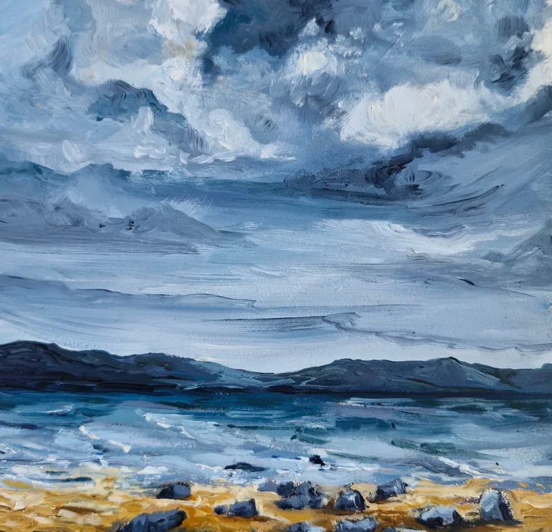 Rolling blue sea under a big stormy sky of white and slate cloud, dark rocks on a strip of yellow sand in the foreground