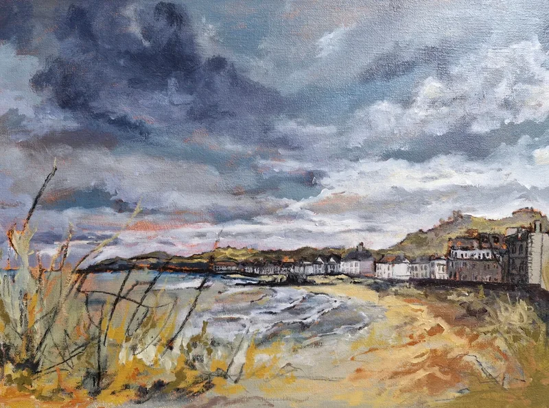 Dune grasses in front of a sandy beach curving towards the white houses of North Berwick, under a dark stormy sky