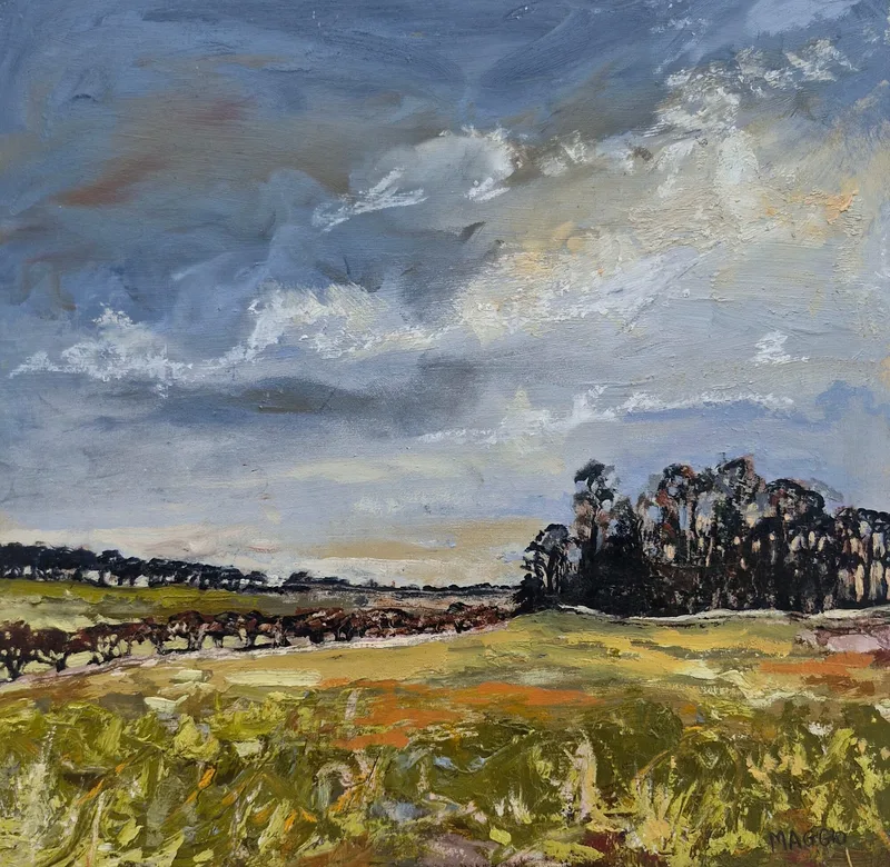 Green spring fields running to a dark clump of trees under a high grey and white sky
